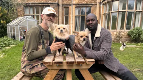 Dwayne Fields sits on the right hand side of a picnic table. Opposite him is Peter, a homeless man, and between them are Peter's two Pekingese chihuahuas who he describes as his only family.