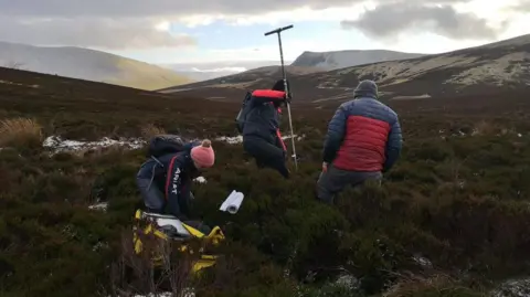 Cumbria Wildlife Trust Three people using equipment to survey the peat on the lower slopes of Skiddaw.