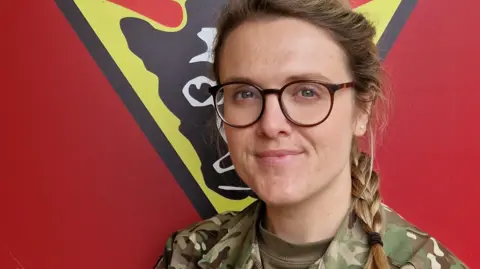Office of the Lieutenant-Governor A female army officer with glasses and long plaited hair, wearing a camouflage army uniform
