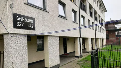 LDRS A block of flats, with a black sign on the left hand corner of the wall which reads 'Shirburn 327 342'