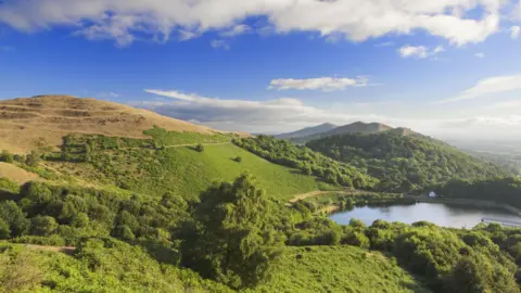 Getty Images A series of large green hills on a sunny but cloudy day with a small reservoir at the bottom of one hill and to the right of the image.