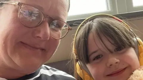 Julie Heron Linda Heron and one of her daughters smiling. The daughter is wearing yellow headphones.