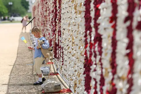 A child with a toy bear and an Ukrainian flag stands before the bear installaton.