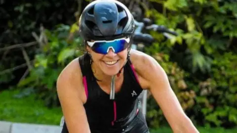 Family Photo Rebecca Comins cycling and grinning with a bike helmet and sunglasses on 