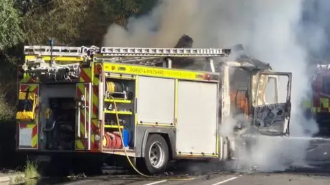 DWFRS The burning fire engine parked on the side of the road. A lot of smoke is coming out.