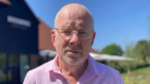 A man in his 70s in a pink shirt and glasses