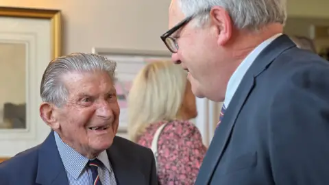 Ernest smiles at a man who is standing next to him