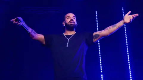Canadian rapper Drake on stage holding a microphone with his arms outstretched