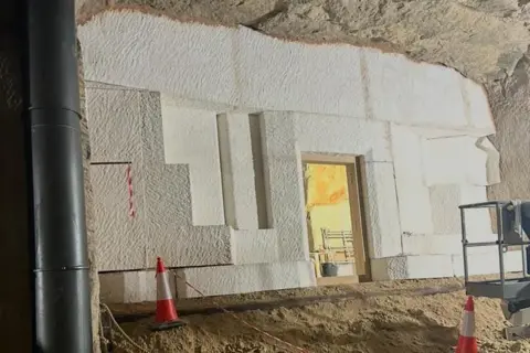 Steve Rogers A view of a set inside the cave/ It shows angular large white brick work built in to the cave surrounding. 