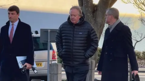 The Duke of Marlborough is seen walking in the middle of two men on their way to High Wycombe Magistrates' Court. He is wearing a dark puffer-style coat - the two men are wearing smart long coats
