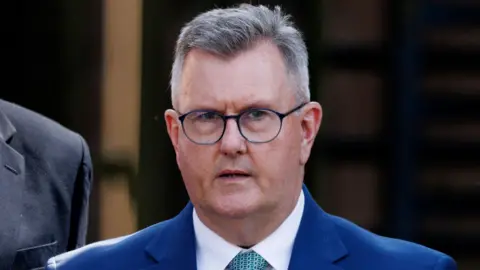 Sir Jeffrey Donaldson leaving Newry Crown Court. He has short grey hair, wearing glasses, a blue blazer, white shirt and light blue tie.