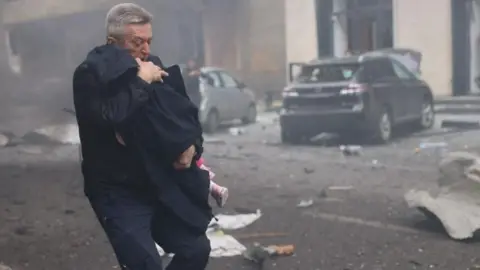 Emergency Services of Ukraine Oleksandr Volobuev carries a young child out of a kindergarten hit by a Russian drone