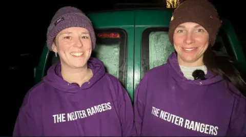 Two woman smiling at the camera wearing purple hoodies which read The Neuter Rangers.