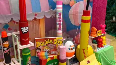 Racks of giant versions of popular sweets including a push pop, a souble dip, a kinder surprise egg, gummy bears and more.