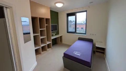 Interior view of one of the new rooms, showing a single bed and built in storage and TV