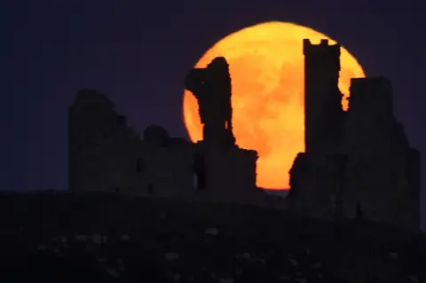 PA Media The Sturgeon Moon over Dunstanburgh Castle in Northumberland