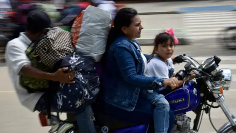 A man, woman and young girl ride a motorcycle through Tibu, Colombia while holding large bags filled with belongings.