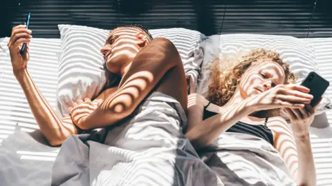 Getty Images Couple lying in bed and using smartphones.