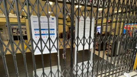 A London Underground station entrance is closed off with metal gates, with Transport for London signs behind them warning of disruption due to RMT strike action.