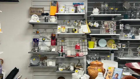 Shelves piled with bric a brac inside a charity shop