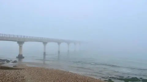 Janie A very foggy coastal scene.  A pier vanishes into the fog at Bembridge. Visibility is very limited and the sky is white. In the foreground you can see a pebble beach and waves gently lapping at the shore.