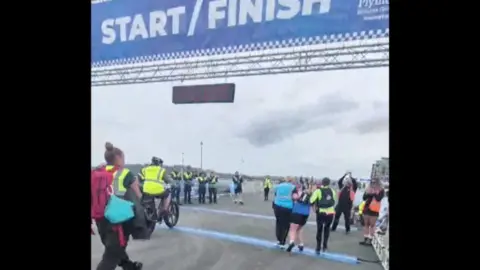 Issy Hart Issy Hart being helped across the line asshe finished the 2026 Plymouth Half Marathon