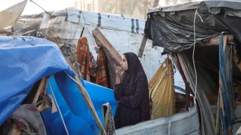 Reuters A Palestinian woman looks on at a tent camp hit by an Israeli air strike in Deir al-Balah, central Gaza (14 January 2024)