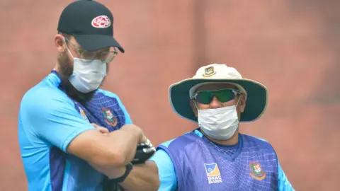 AFP Bangladesh cricket team head coach Russell Domingo (R) and bowling coach Daniel Vettori wearing face masks watch the team during a practice session at Arun Jaitley Cricket Stadium in Delhi on November 1, 2019,