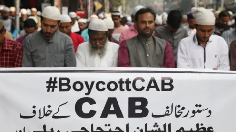 Reuters Protesters offering Friday prayers in front of a banner reading #BoycottCAB