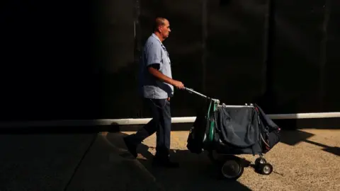 Reuters A US postal worker pushes a mail cart