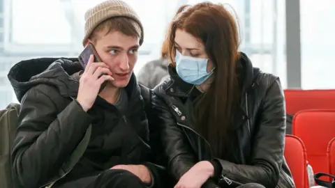 Getty Images A young woman wearing a face mask looks at her unmasked partner at a train station in the Russian city of Sochi