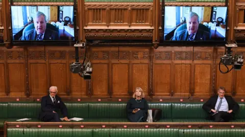 UK Parliament MPs sit in the chamber listening to a colleague on Zoom