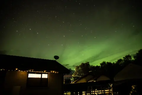 Dave Stewart A green tinted aurora filling a starry sky above a house at night