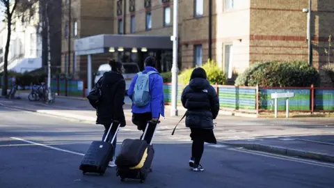 Three asylum seekers wirth luggage move out from a Home Office contracted London hotel