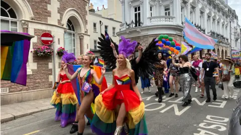 A group of people at the Pride event in Jersey wearing colourful outfits and holding flags.