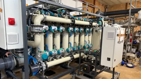 Matt Day A white microfiltration plant is across the image and is made of multiple pipes. There are two white boxes either side of the image. 