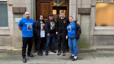 Five people outside a court building. Some of them have blue t-shirts on with Tyran's picture on them.