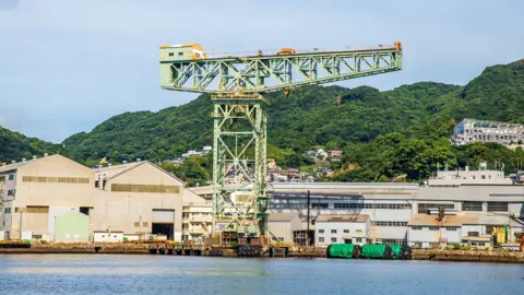 Getty Images A steel latticed crane, painted in light green with industrial buildings and hills in the background