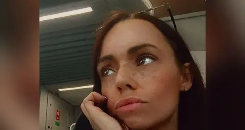 A photograph issued by police of Jade Downes. She has brown eyes and long brown hair and is resting her face in her hand, looking thoughtful.
