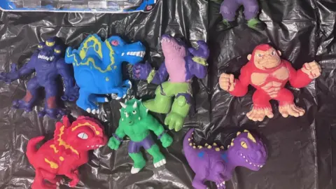 Isabella A collection of small figurines of monsters, dinosaurs and animals laid out on a black plastic bin bag