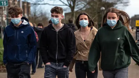 Getty Images Four students walking side-by-side wearing blue face masks. Two boys on the left of the image, two girls on the right.