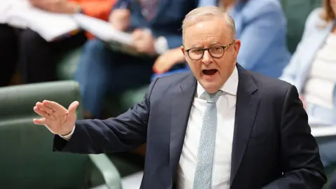 Getty A middle aged man with thinning grey hair and glasses, wearing a suit and tie, gestures as he addresses parliament