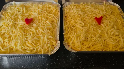 Rebecca Harrington Two lasagnes in foil trays with grated cheese on top and a heart in the middle