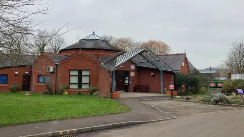 A GP surgery's main entrance, with some grass and a road
