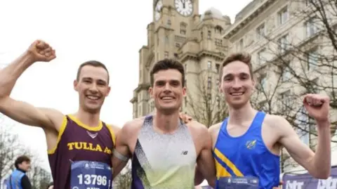 BTR Liverpool Jack Bromley stand in centre with Meehan and Wootton on either side of him raising their hands. The Liver Building looms behind them.
