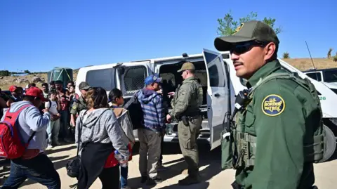 Getty Images Agen Bea Cukai dan Patroli Perbatasan memuat migran ke dalam kendaraan setelah sekelompok migran masuk ke AS dari Meksiko di Jacumba Hot Springs, California, pada 5 Juni 2024. 