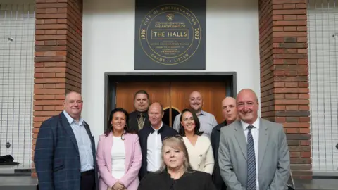 Wolverhampton City Council Nine people assemble for a photo in front of a door, above which is a black-coloured square plaque with golden writing. 