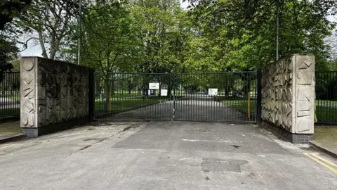 The closed gates of Hull's East Park made of black metal bars with concrete patterned walls on either side