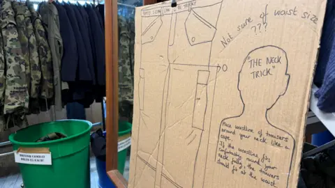 A picture of a notice in a military surplus store which says if someone is not sure of the waist size of trousers to use a trick to wrap the trouser waist around their neck and if it fits it should fit their waist, the sign also says Nato sizing can be tricky.