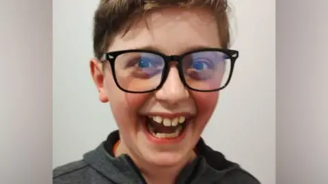 Kyle Sieniawski, laughing. Kyle has a huge smile, large black-rimmed glasses and wears a grey hooded top.